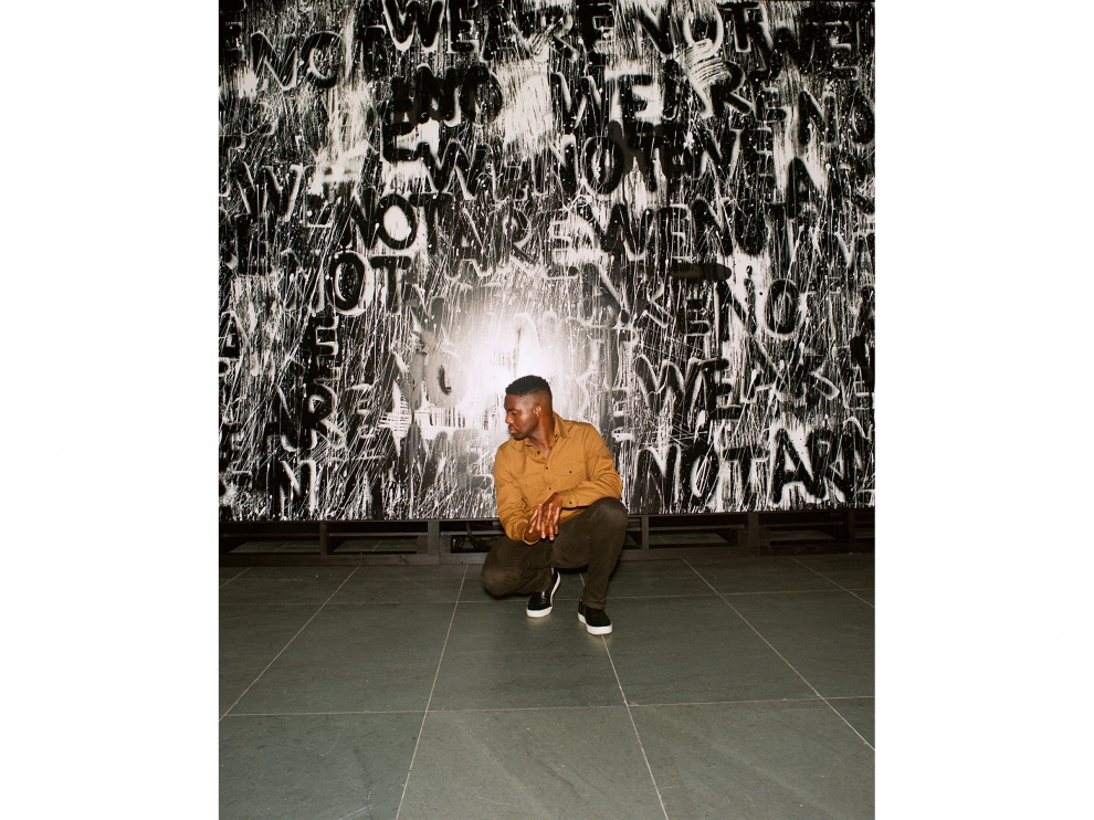 Photograph of Adam Pendleton crouching in front of one of his silkscreen artworks